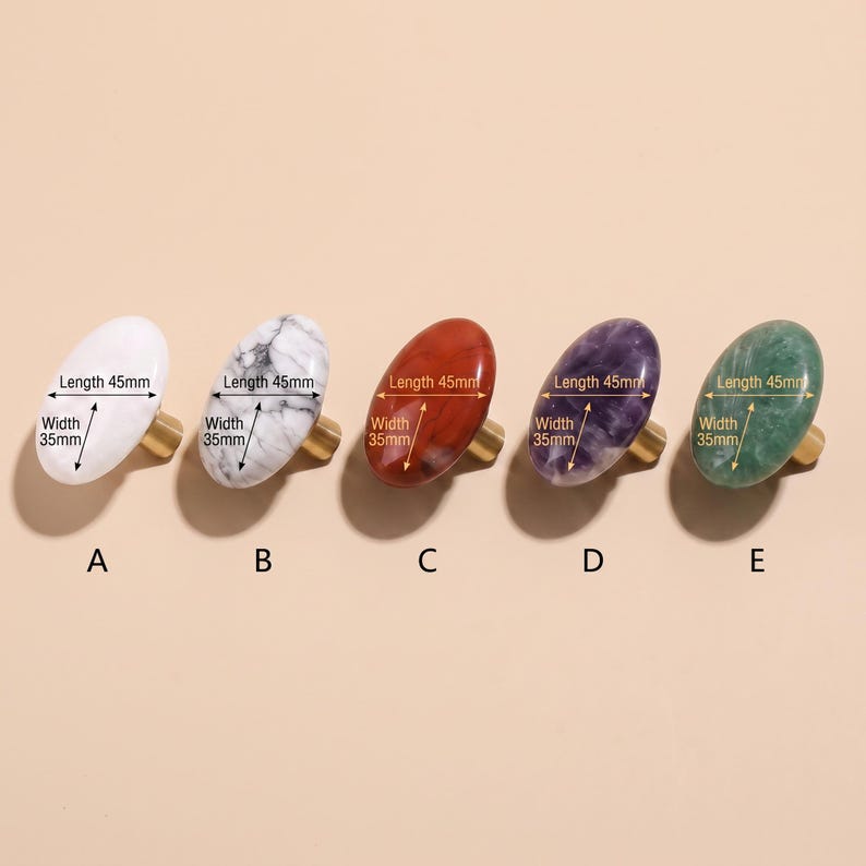 May include: Five oval cabinet knobs labelled A through E, each with a gold-tone metal base. The knobs feature different finishes: solid white, white marble, reddish-brown, purple, and green. Each knob measures 45mm in length and 35mm in width.
