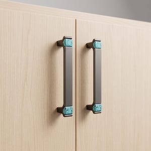 Peut inclure: Deux poign&eacute;es de placard verticales en m&eacute;tal gris fonc&eacute; avec des incrustations rectangulaires en pierre turquoise aux extr&eacute;mit&eacute;s sup&eacute;rieure et inf&eacute;rieure. Les poign&eacute;es sont fix&eacute;es sur des portes en bois clair &agrave; grain vertical.