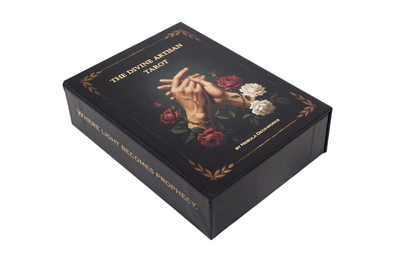 May include: A black tarot card box with gold lettering reading "THE DIVINE ARTISAN TAROT". The box features an illustration of two hands intertwined, surrounded by red and white roses. The text "WHERE LIGHT BECOMES PROPHECY" is also visible.