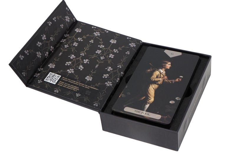 May include: A black tarot card box with a floral design on the inner lid. Inside, tarot cards feature a vintage illustration of a person in a yellow outfit. The card is labelled "THE FOOL".