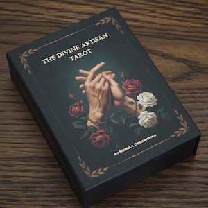May include: A black tarot card box with the title "THE DIVINE ARTISAN TAROT" in gold lettering. The box features an illustration of clasped hands surrounded by red and white roses. The box is on a wooden surface.