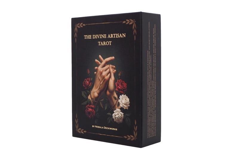 May include: A black tarot card box with the title "THE DIVINE ARTISAN TAROT" in gold lettering. The box features an illustration of clasped hands surrounded by red and white roses. The box is rectangular and has gold decorative accents.