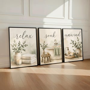 May include: A set of three framed wall art prints featuring watercolor illustrations of bathroom scenes. The prints display the words relax, soak, and unwind in black script, accompanied by images of a vase, a bathtub, and a soap dispenser.