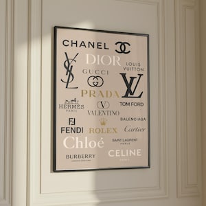 May include: A rectangular wall art print in a black frame featuring a beige background with various luxury fashion brand logos and names in black, white, and gold text, including Chanel, Dior, Gucci, Louis Vuitton, Prada, Hermes, and Fendi.