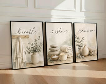 May include: Three framed wall art prints featuring spa-themed imagery. The first print shows a robe and a vase with greenery and the word "breathe". The second shows stacked stones, a candle, and towels with "restore". The third shows a vase and towels with "renew".