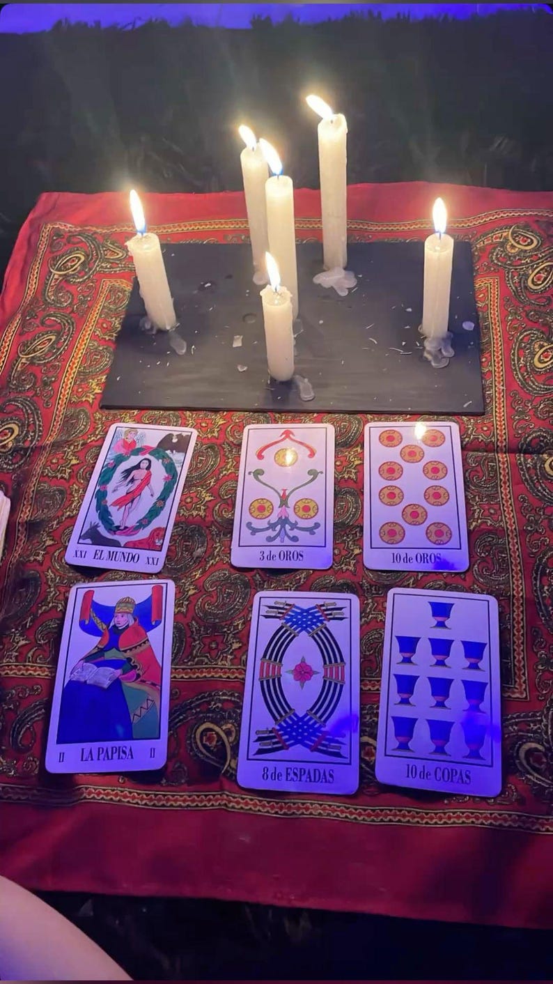 K&ouml;nnte beinhalten: Sechs wei&szlig;e Kerzen stehen auf einer schwarzen rechteckigen Schieferplatte, angeordnet &uuml;ber sechs Tarotkarten auf einem roten Tuch mit Paisleymuster. Die Karten sind mit El Mundo, 3 de Oros, 10 de Oros, La Papisa, 8 de Espadas und 10 de Copas beschriftet.
