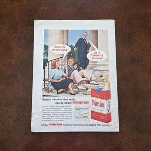 Puede incluir: Un anuncio de revista antiguo de cigarrillos Winston con un hombre y una mujer sentados en escalones de piedra y un hombre detr&aacute;s. El texto dice WINSTON TASTES GOOD! AS A CIGARETTE SHOULD! e incluye una cajetilla de cigarrillos Winston roja.