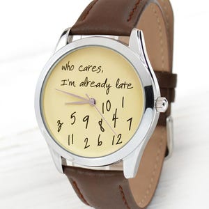 May include: A wristwatch with a silver-colored case and a brown leather band. The watch face is cream-colored with black numerals and the text "who cares, I'm already late". The watch hands are silver.