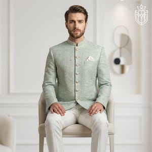 K&ouml;nnte beinhalten: Hellgr&uuml;ne Jacke mit Stehkragen und goldenen Kn&ouml;pfen, kombiniert mit einer wei&szlig;en Hose. Die Jacke hat ein dezentes geometrisches Muster und ein Einstecktuch. Das Outfit ist formell und elegant.