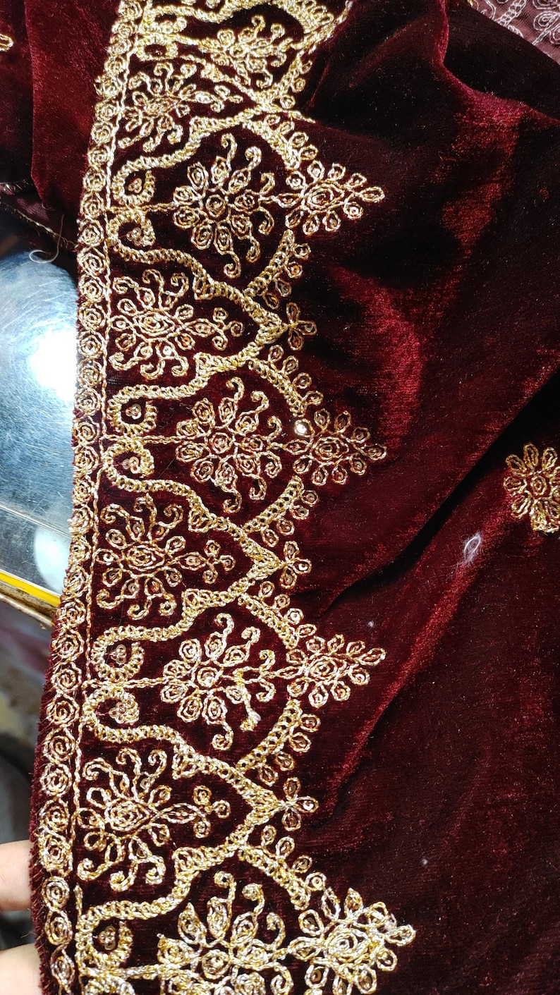 May include: A deep burgundy velvet fabric featuring an intricate border of metallic gold embroidery. The design consists of repeating floral motifs enclosed within scalloped arches, with additional small floral patterns scattered across the velvet.