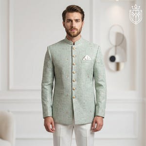 K&ouml;nnte beinhalten: Hellgr&uuml;ne Jacke mit Stehkragen und goldenen Kn&ouml;pfen. Die Jacke hat ein geometrisches Muster und ein Einstecktuch. Sie wird mit einer wei&szlig;en Hose getragen. Der Stil ist formell und elegant.