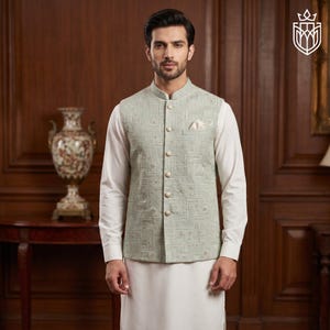 May include: A light green embroidered vest with a mandarin collar and button closure, worn over a white long-sleeved shirt and white pants. The vest features a geometric pattern and a pocket square. The outfit is formal wear.