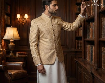 Könnte beinhalten: Eine goldfarbene, langärmelige Jacke mit Stehkragen, dezentem Blumenmuster und einer Knopfleiste, getragen über einer schlichten weißen Tunika. Die Jacke hat eine strukturierte Passform und ein Einstecktuch, präsentiert in einer Bibliothek.