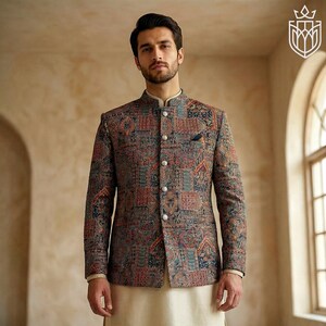 May include: A patterned jacket with a mandarin collar, featuring a patchwork design in shades of red, blue, and brown. The jacket has a pocket square and button closures. The model is wearing a cream-colored shirt and pants.
