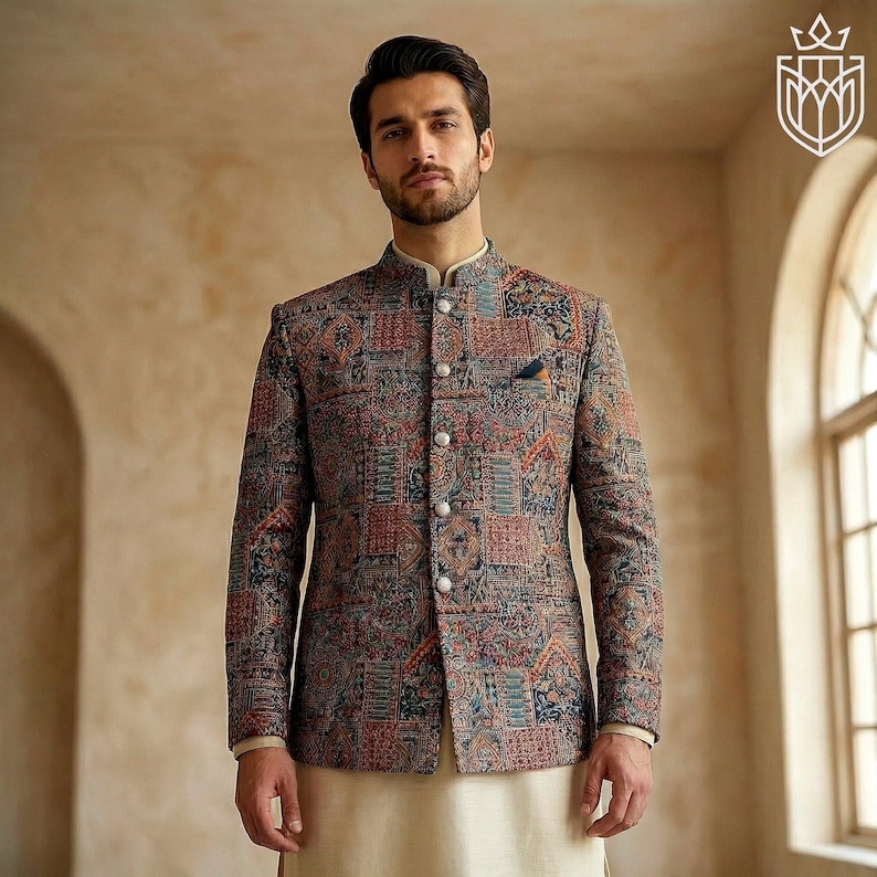 May include: A patterned jacket with a mandarin collar, featuring a patchwork design in shades of red, blue, and brown. The jacket has a pocket square and button closures. The model is wearing a cream-colored shirt and pants.