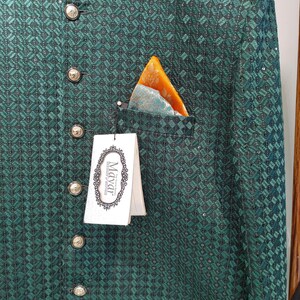 May include: Emerald green jacket with a geometric pattern, featuring gold-colored buttons and a pocket square with orange and teal accents. The jacket has a high collar and a tag that reads "Mayar".