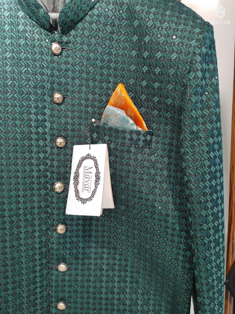 May include: Emerald green jacket with a geometric pattern, featuring gold-colored buttons and a pocket square with orange and teal accents. The jacket has a high collar and a tag that reads "Mayar".