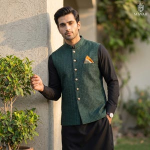 May include: A dark green textured vest with gold buttons and a matching pocket square. The vest is worn over a black long-sleeve shirt and paired with black pants. The image includes the logo "MAYAR".