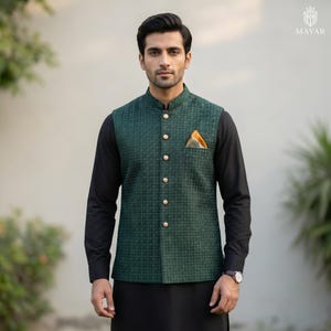 May include: A dark green vest with a houndstooth pattern, featuring gold buttons and a mandarin collar. The vest has a pocket square with orange and yellow accents. The vest is worn over a black long-sleeve shirt and black pants.