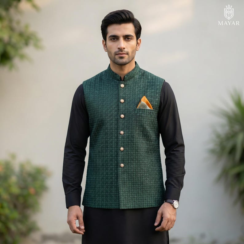 May include: A dark green vest with a houndstooth pattern, featuring gold buttons and a mandarin collar. The vest has a pocket square with orange and yellow accents. The vest is worn over a black long-sleeve shirt and black pants.