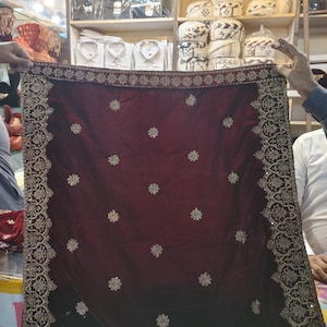 May include: A deep maroon velvet shawl featuring an intricate gold embroidered border and scattered gold floral motifs across the fabric. The rectangular textile displays a dense, ornate pattern along all four edges with small, repeating flower designs.