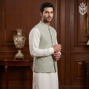 May include: A light green vest with a geometric pattern, worn over a white long-sleeve shirt and white pants. The vest has a mandarin collar and gold-colored buttons. The outfit is formal and elegant.