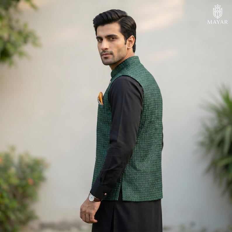 May include: A green textured vest with a black long-sleeve shirt and black pants. A yellow pocket square is visible in the vest pocket. The person is wearing a watch with a silver band.