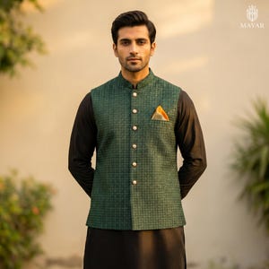 May include: A green patterned vest with gold buttons and a pocket square. The vest is worn over a black long-sleeve shirt and black pants. The vest has a houndstooth pattern.