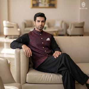 May include: A burgundy patterned vest with gold buttons over a black long-sleeve shirt. The vest has a floral design. The person is wearing black pants and a white pocket square. The logo "MAYAR" is in the top right corner.