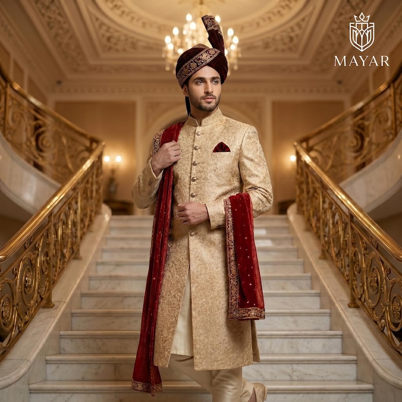 May include: A gold sherwani with intricate embroidery, a matching turban, and a deep red velvet stole. The garment features a high collar, a button-down front, and a pocket square. The Mayar logo is visible in the top right corner of the image.