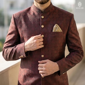 May include: A dark maroon bandhgala jacket featuring a subtle tonal paisley pattern, a mandarin collar, and a row of five gold-toned buttons down the front. The jacket includes a chest pocket with a beige pocket square and three buttons on each cuff.