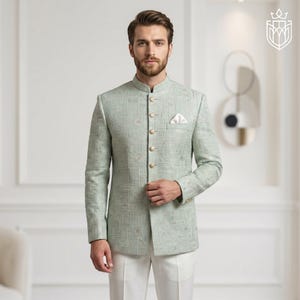 K&ouml;nnte beinhalten: Hellgr&uuml;ne Jacke mit Stehkragen und goldenen Kn&ouml;pfen. Die Jacke hat ein dezentes geometrisches Muster und wird mit einer wei&szlig;en Hose kombiniert. Ein wei&szlig;es Einstecktuch ist sichtbar. Das Outfit ist formell und elegant.