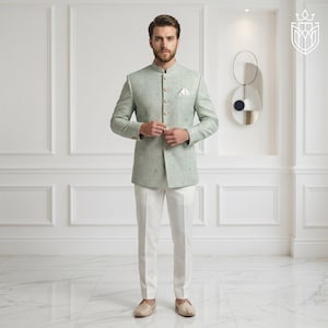 K&ouml;nnte beinhalten: Ein hellgr&uuml;ner Anzug mit Stehkragen, kombiniert mit einer wei&szlig;en Hose. Das Jackett hat ein strukturiertes Muster und ein Einstecktuch. Das Outfit wird durch beige Loafer abgerundet. Der Hintergrund ist eine wei&szlig;e Wand mit dekorativen Leisten.