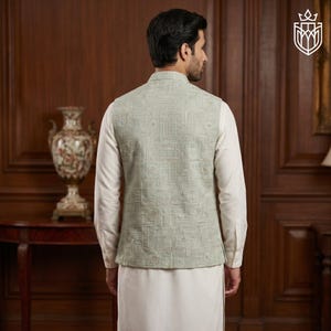 May include: A light green vest with a geometric pattern, worn over a white long-sleeve shirt and white pants. The vest has a mandarin collar and a detailed design. The outfit is suitable for formal occasions.