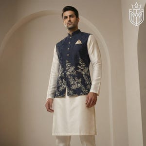 May include: A man wearing a navy blue vest with a floral pattern over a white long-sleeved shirt and cream-colored pants. The vest has gold-colored buttons and a small pocket square. The outfit is formal and elegant.