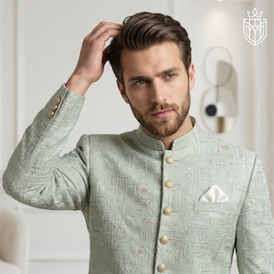 K&ouml;nnte beinhalten: Hellgr&uuml;ne Jacke mit geometrischem Muster und goldenen Kn&ouml;pfen. Die Jacke hat einen Stehkragen und ein Einstecktuch. Teil einer formellen Bekleidungskollektion.