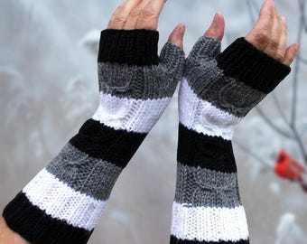 May include: A pair of fingerless gloves in black, white and grey stripes. The gloves are knitted and feature a cable knit pattern.