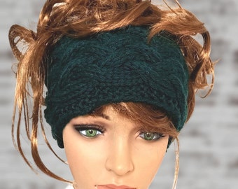 May include: A dark green knitted headband with a cable knit pattern. The headband is worn by a person with long, curly, reddish-brown hair.