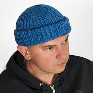 May include: A blue knitted beanie with a ribbed texture. The beanie has a folded brim and is made of a soft, warm material.