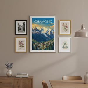 May include: A gallery wall featuring framed art prints. The central piece is a poster with the text "CHAMONIX France" depicting a mountain scene. Other frames display botanical illustrations and a monochrome street view. The wall is painted in a neutral tone.