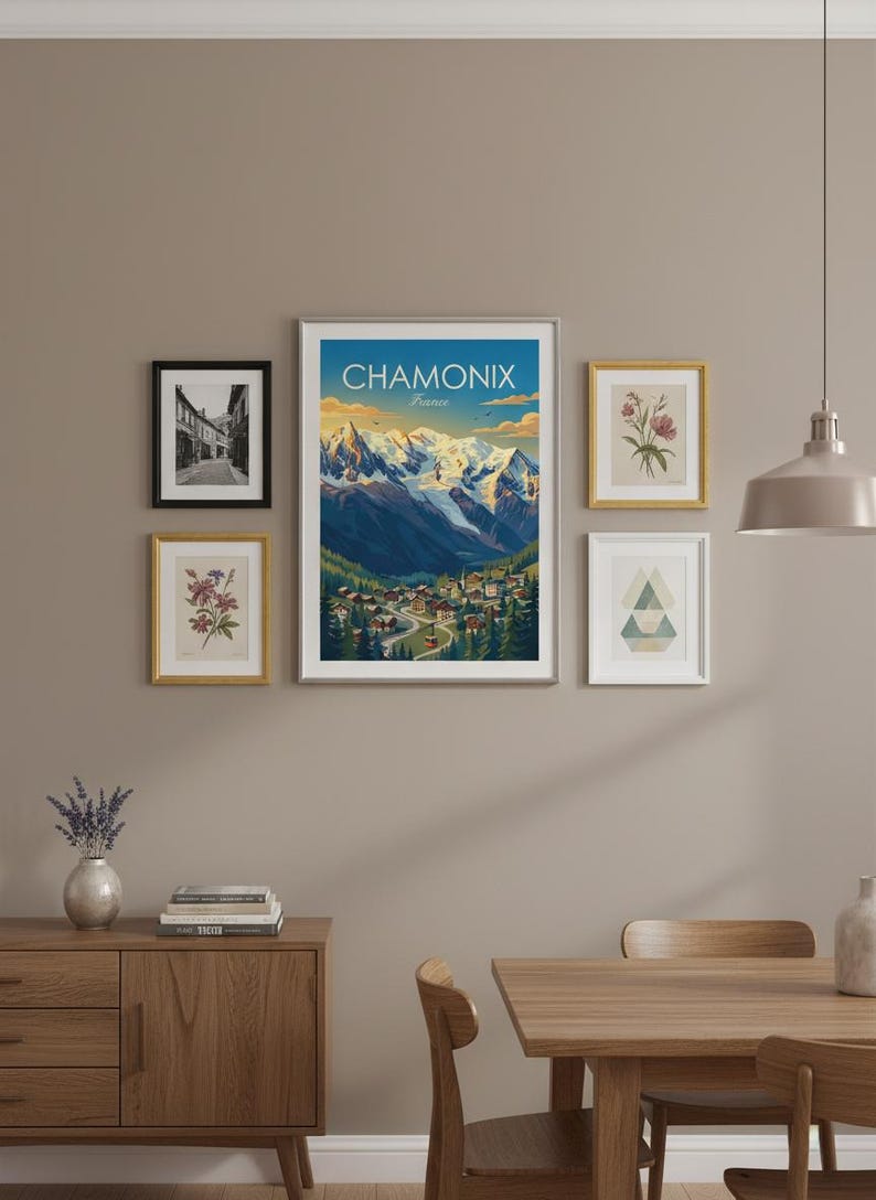 May include: A gallery wall featuring framed art prints. The central piece is a poster with the text "CHAMONIX France" depicting a mountain scene. Other frames display botanical illustrations and a monochrome street view. The wall is painted in a neutral tone.