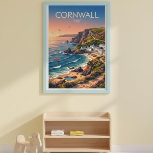 May include: A framed print of Cornwall, UK, featuring a coastal landscape with a beach, cliffs, and a small town. The artwork has a blue frame and depicts a sunset with an orange boat on the water. The text "Cornwall UK" is at the top.