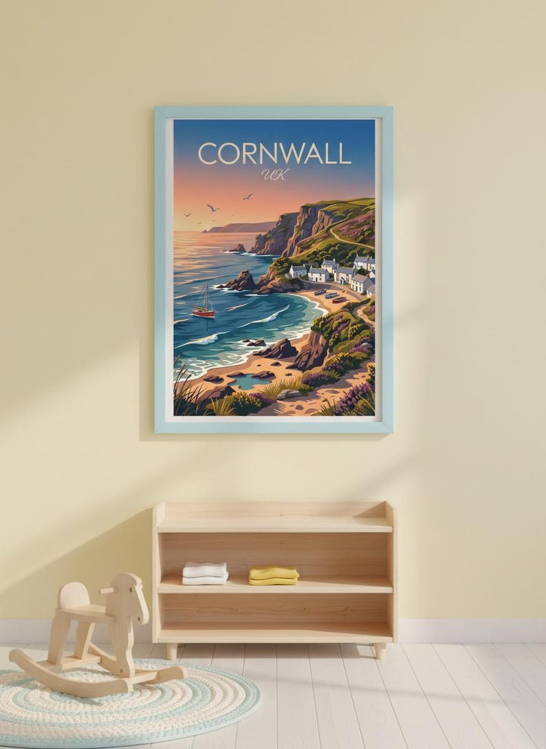 May include: A framed print of Cornwall, UK, featuring a coastal landscape with a beach, cliffs, and a small town. The artwork has a blue frame and depicts a sunset with an orange boat on the water. The text "Cornwall UK" is at the top.