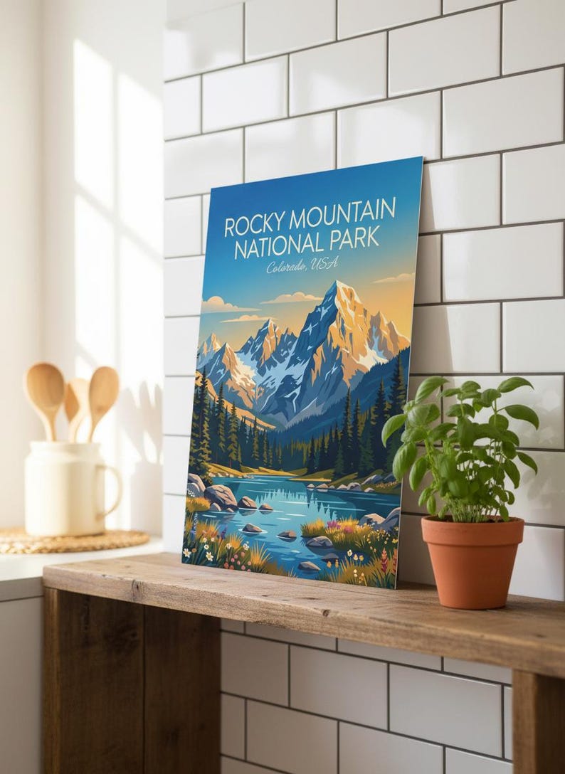 May include: A framed print featuring the Rocky Mountain National Park in Colorado, USA. The image shows a mountain range with snow-covered peaks, a lake, and evergreen trees. The sky transitions from blue to yellow.