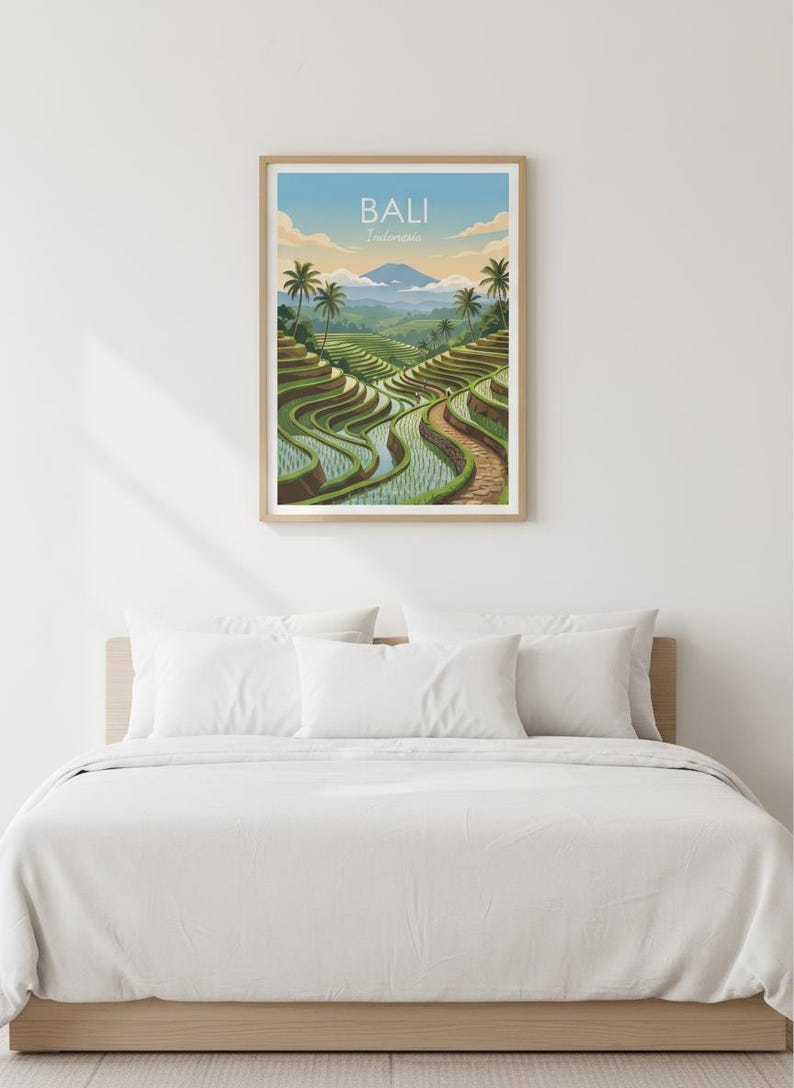 May include: A framed print featuring a scenic view of Bali, Indonesia. The artwork depicts lush green rice terraces, winding pathways, and palm trees under a blue sky. The print is displayed above a bed with white bedding.