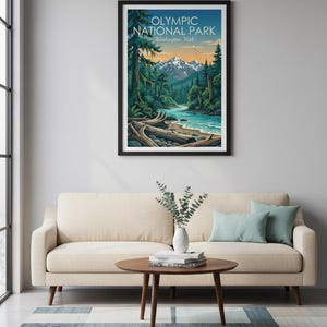 May include: A framed art print featuring a vibrant landscape of Olympic National Park in Washington, USA. The artwork depicts a river flowing through a forest with mountains in the background. The print is displayed above a beige sofa with teal pillows.