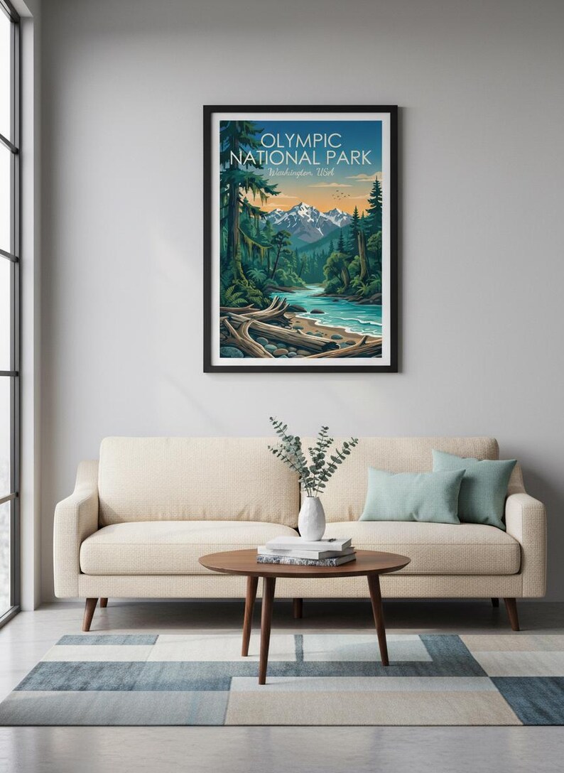 May include: A framed art print featuring a vibrant landscape of Olympic National Park in Washington, USA. The artwork depicts a river flowing through a forest with mountains in the background. The print is displayed above a beige sofa with teal pillows.