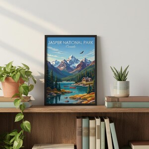 May include: A framed art print of Jasper National Park in Canada. The artwork depicts a serene lake scene with mountains, trees, and a small cabin. The sky is blue with a soaring bird. The print is displayed on a wooden shelf with books and plants.