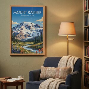 May include: A framed print of Mount Rainier in Washington, USA, hangs on a green wall. The artwork depicts a mountain landscape with a river, flowers, and a blue sky. A blue armchair with a throw blanket and pillow sits below the print.