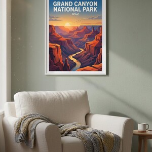 May include: A framed art print of the Grand Canyon National Park in the USA. The artwork depicts a stylized landscape with a river winding through red rock formations under a sunset sky. The print is in a white frame.